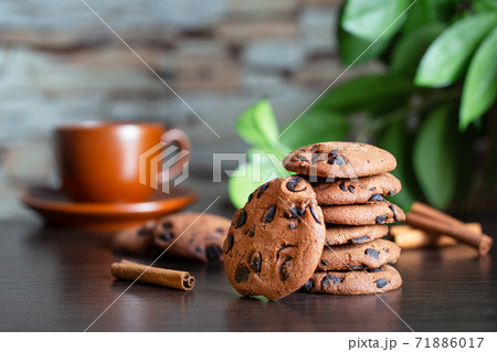Oatmeal cookies with chocolate on the table against background of cup of coffee and green leaves Oatmeal cookies with chocolate on the table against background of cup of coffee and green leaves 71886017