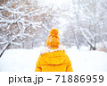 Back view of young woman wearing yellow jacket walks in snowy park 71886959