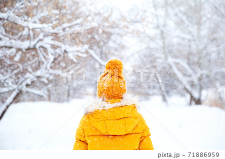Back view of young woman wearing yellow jacket walks in snowy park 71886959