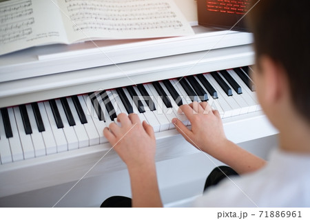 Hands of a boy playing the piano with sheet music. 71886961