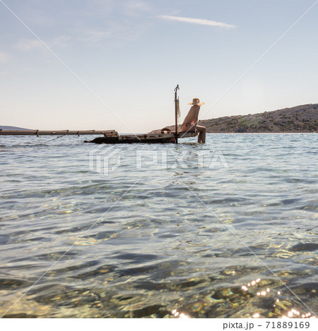 View of unrecognizable woman wearing big summer sun hat tanning topless and relaxing on old wooden pier in remote calm cove of Adriatic sea, Croatia View of unrecognizable woman wearing big summer sun hat tanning topless and relaxing on old wooden pier in remote calm cove of Adriatic sea, Croatia 71889169