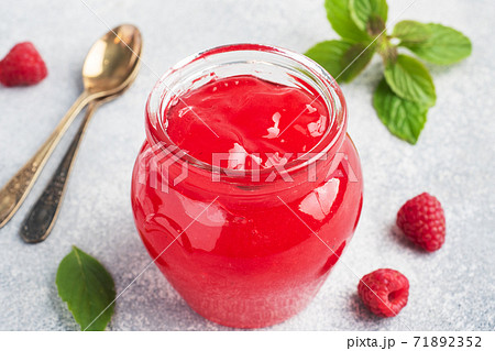 Homemade raspberry jam in a glass jar and fresh raspberries with mint on a grey concrete background. Copy space Homemade raspberry jam in a glass jar and fresh raspberries with mint on a grey concrete background. Copy space 71892352