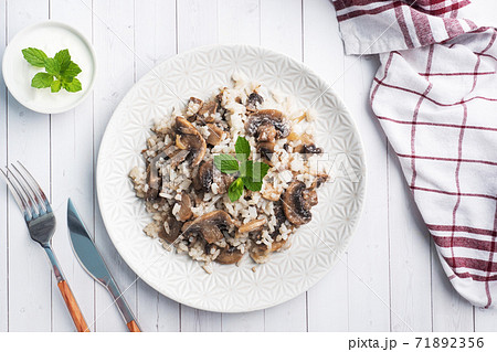 Risotto with mushrooms on a white plate. Boiled white rice with champignons in cream sauce. Light wooden background. Copy space 71892356