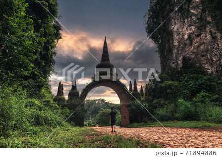 Khao Na Nai Luang Dharma Park, Suratthani, Thailand. Tourist man walking to ancient arch gate with colorful sky Khao Na Nai Luang Dharma Park, Suratthani, Thailand. Tourist man walking to ancient arch gate with colorful sky 71894886