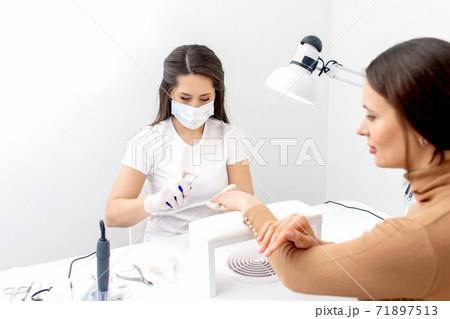Manicurist is appies spray on client hand. 71897513