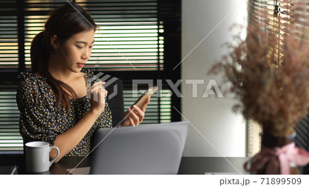 Businesswoman using smartphone while sitting in office room 71899509