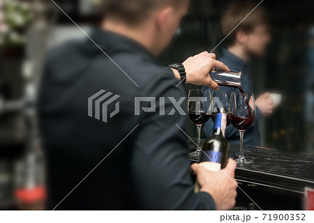 Barman pouring red wine into glasses in detail 71900352