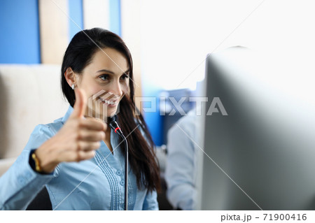 Smiling woman looks at monitor and holds her thumbs up. 71900416