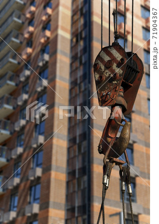Construction crane hook with multi-storey building under construction (new residential complex) on the background. Construction site upon renovation program in Cheryomushki district, Moscow, Russia Construction crane hook with multi-storey building under construction (new residential complex) on the background. Construction site upon renovation program in Cheryomushki district, Moscow, Russia 71904367