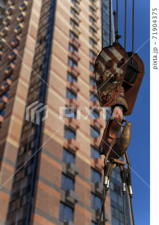 Construction crane hook with multi-storey building under construction (new residential complex) on the background. Construction site upon renovation program in Cheryomushki district, Moscow, Russia Construction crane hook with multi-storey building under construction (new residential complex) on the background. Construction site upon renovation program in Cheryomushki district, Moscow, Russia 71904375