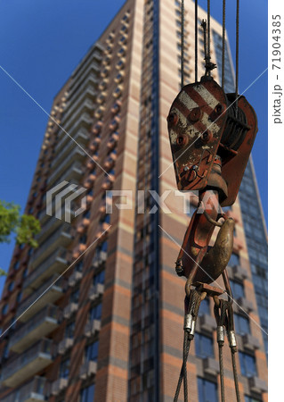 Construction crane hook with multi-storey building under construction (new residential complex) on the background. Construction site upon renovation program in Cheryomushki district, Moscow, Russia Construction crane hook with multi-storey building under construction (new residential complex) on the background. Construction site upon renovation program in Cheryomushki district, Moscow, Russia 71904385
