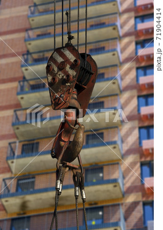 Construction crane hook with multi-storey building under construction (new residential complex) on the background. Construction site upon renovation program in Cheryomushki district, Moscow, Russia Construction crane hook with multi-storey building under construction (new residential complex) on the background. Construction site upon renovation program in Cheryomushki district, Moscow, Russia 71904414