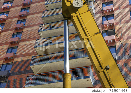 Part of a construction machine (excavator or crane) with multi-storey building under construction (new residential complex) on the background, Moscow, Russia Part of a construction machine (excavator or crane) with multi-storey building under construction (new residential complex) on the background, Moscow, Russia 71904443