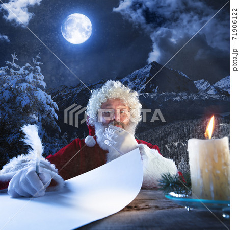 Emotional Santa Claus congratulating with New Year and Christmas, writing a letter, wish list in midnight with candle 71906122