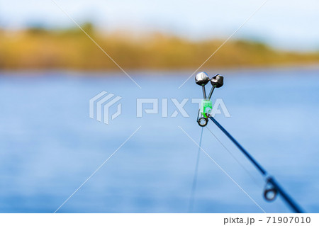 Fishing rod with a bell on the background of the river. Fishing hobby 71907010