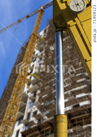 Part of a construction machine (excavator or crane) with multi-storey building under construction with scaffolding (new residential complex) on the background, Moscow, Russia 71908123