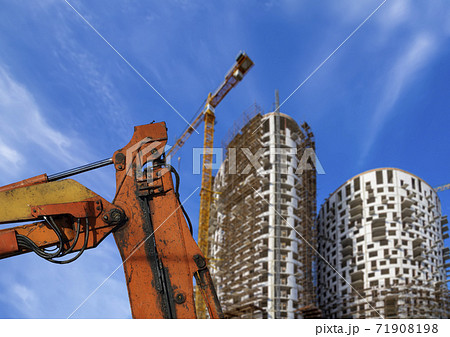 Part of a construction machine (excavator or crane) with multi-storey building under construction with scaffolding (new residential complex) on the background, Moscow, Russia 71908198