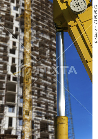 Part of a construction machine (excavator or crane) with multi-storey building under construction with scaffolding (new residential complex) on the background, Moscow, Russia Part of a construction machine (excavator or crane) with multi-storey building under construction with scaffolding (new residential complex) on the background, Moscow, Russia 71909071