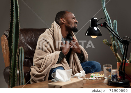Young African-american man wrapped in a plaid looks sick, ill, sitting at home indoors. Healthcare concept 71909696