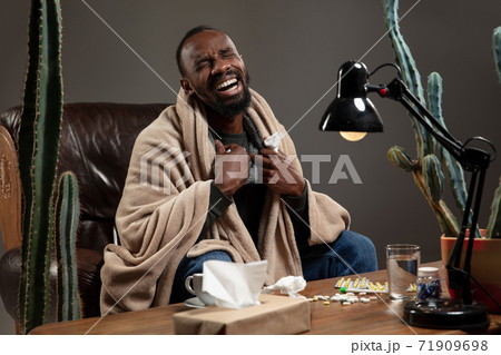 Young African-american man wrapped in a plaid looks sick, ill, sitting at home indoors. Healthcare concept 71909698