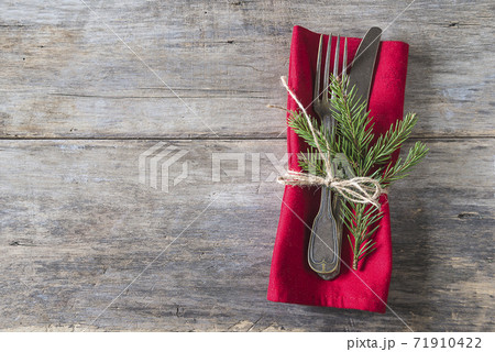 Christmas holiday table setting. Vintage fork and knife, fir twig on red napkin and old non paint wooden background. Space for text, top view Christmas holiday table setting. Vintage fork and knife, fir twig on red napkin and old non paint wooden background. Space for text, top view 71910422