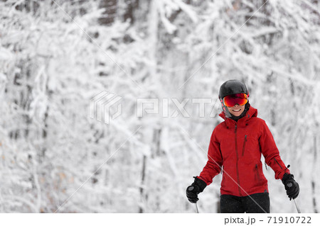 Winter sport happy skier Alpine skiing going dowhill against snow covered trees background during winter snowstorm. Woman in red jacket and goggles Winter sport happy skier Alpine skiing going dowhill against snow covered trees background during winter snowstorm. Woman in red jacket and goggles 71910722