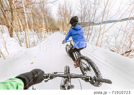 Couple biking on fat bikes on winter snow trail outdoor. Mountain nature landscape, woman rider cycling from behind with point of view of man holding handlebar of his bike 71910723
