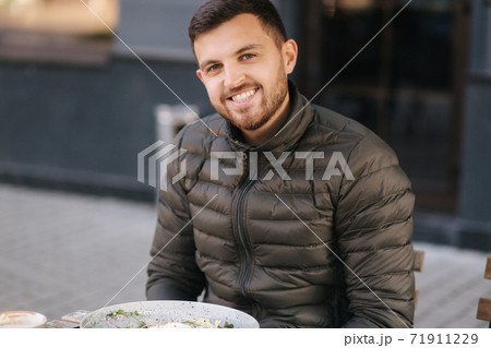 Handsome man sitting outdoors in cafe on terrace and smiled to camera Handsome man sitting outdoors in cafe on terrace and smiled to camera 71911229