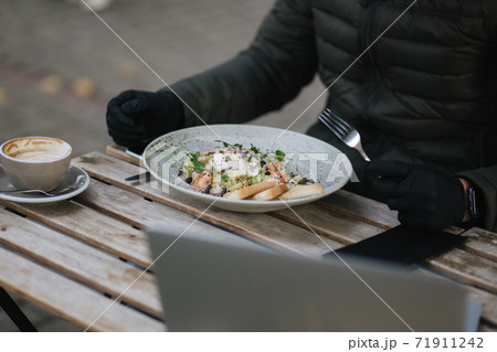 Close up of man in black gloves hold cutlery. Cafe concept during qurantine. Food outdoors in protective gloves. Fresh vegan salad with shrimps 71911242