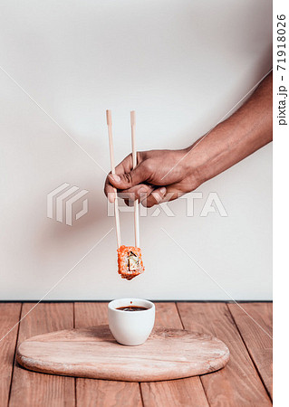 Hand in rubber glove hold sushi with chopstick over a bowl of soy sauce on a white background. Sushi menu. 71918026