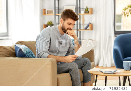 man with bills counting on calculator at home man with bills counting on calculator at home 71923485