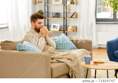 sick young man in blanket with hot tea at home sick young man in blanket with hot tea at home 71924747