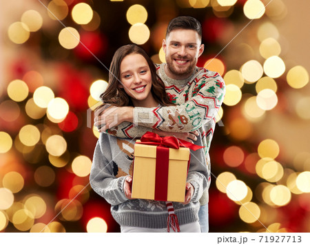 happy couple in christmas sweaters with gift box happy couple in christmas sweaters with gift box 71927713