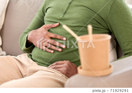 close up of overeaten man and cup of takeaway food 71929291