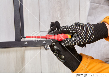 A worker assembles a metal frame for furniture using screwdriver. A worker assembles a metal frame for furniture using screwdriver. 71929660