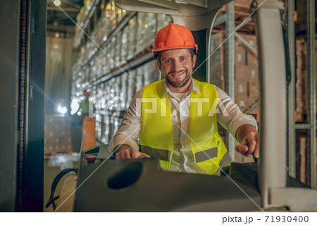 Young bearded worker sitting at the loader and smiling 71930400