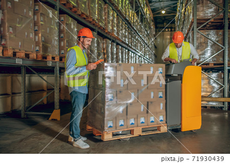Male warehouse workers in helmets standing near containers Male warehouse workers in helmets standing near containers 71930439