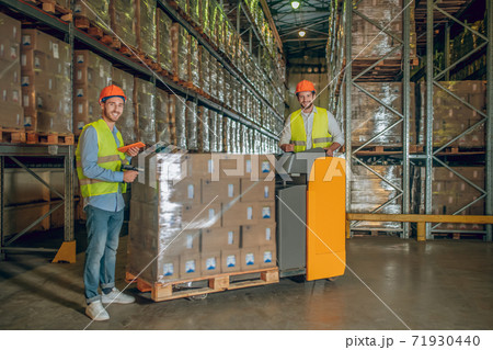 Male warehouse workers in helmet scanning barcodes on the boxes Male warehouse workers in helmet scanning barcodes on the boxes 71930440