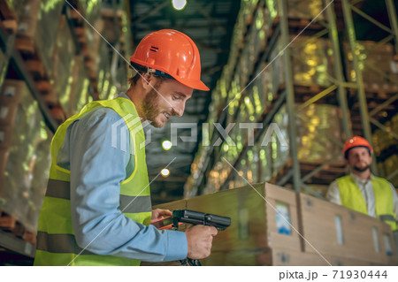 Male warehouse worker in helmet scanning barcodes on the boxes 71930444