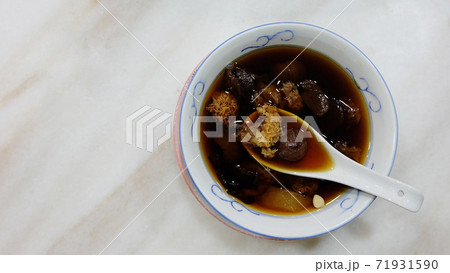 Chinese white fungus and longan sweet soup, in a bowl with Chinese soup spoon, placed on a marble table. Top view. 71931590