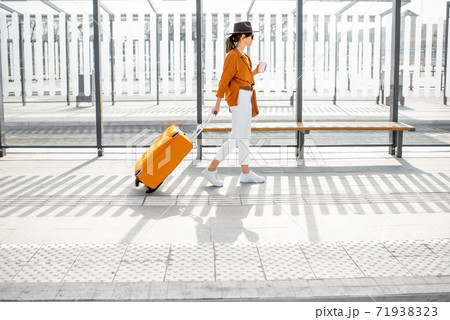Young female traveler with a suitcase at the transport stop 71938323