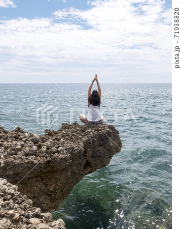 Rear view of young woman with long hair practicing yoga on rocks at sea Rear view of young woman with long hair practicing yoga on rocks at sea 71938820