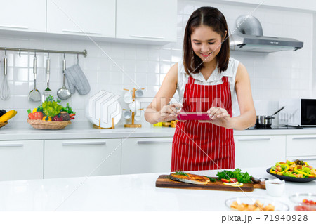 Asian woman chef in red apron take a picture of salmon steak with smartphone. Concept woman preparing meals at home. 71940928