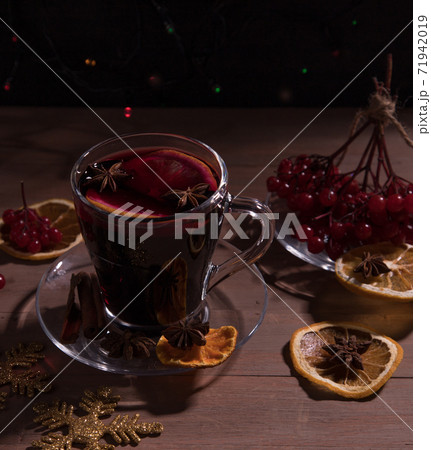 A Cup of hot mulled wine with spices, decorations for the New year, branches of red berries, dark background. Horizontal orientation. A Cup of hot mulled wine with spices, decorations for the New year, branches of red berries, dark background. Horizontal orientation. 71942019