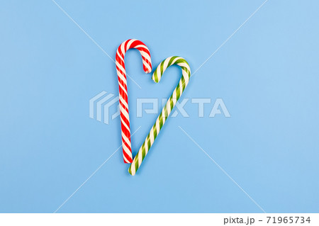 Two Mint hard candy canes striped in Christmas colours on blue background. Closeup. Heart sign Two Mint hard candy canes striped in Christmas colours on blue background. Closeup. Heart sign 71965734