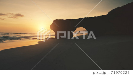 Sun silhouette of rock wall with giant hole on sand beach aerial view. Seascape of ocean cliff coast Sun silhouette of rock wall with giant hole on sand beach aerial view. Seascape of ocean cliff coast 71970222