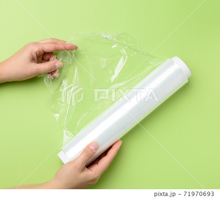 two female hands hold a roll of transparent cling film for packaging products 71970693