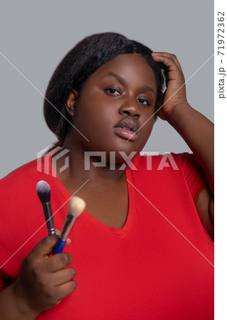 Young dark-skinned woman in red clothes holding brushes for make up. Young dark-skinned woman in red clothes holding brushes for make up. 71972362
