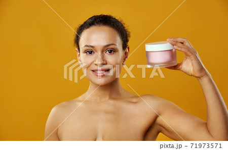 Beautiful african woman holding jar of moisturizer near face isolated on yellow Beautiful african woman holding jar of moisturizer near face isolated on yellow 71973571