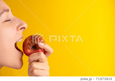 The girl bites a rotten apple with a worm on a yellow background. Expired products, junk food The girl bites a rotten apple with a worm on a yellow background. Expired products, junk food 71973810